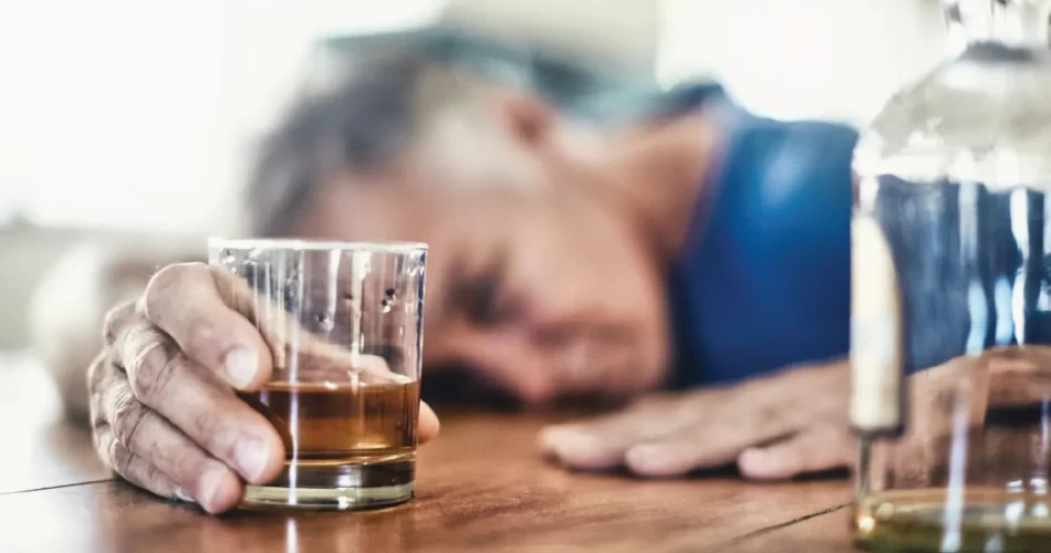 Drunk sleeping on desk holding a glass of alchohol