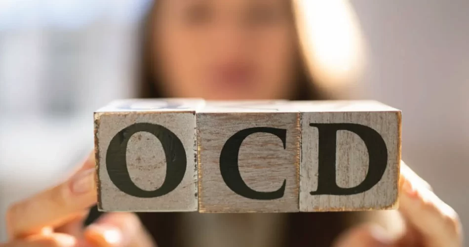 Blurry female in background holding wooden cubes spelling " OCD "