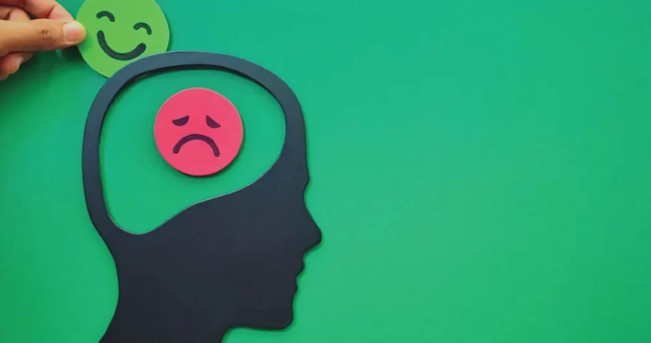 Paper illustration of human a human head with red-sad paper emoji and hand inserting happy-green paper emoji