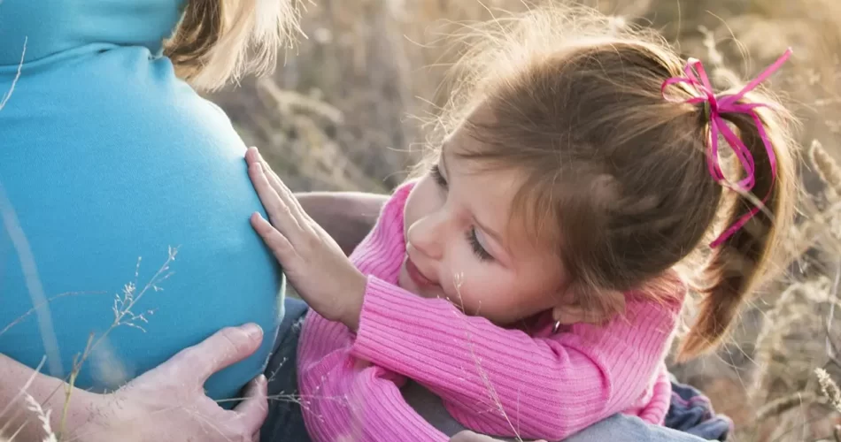 Little girl touching her mother's pregnant stomach